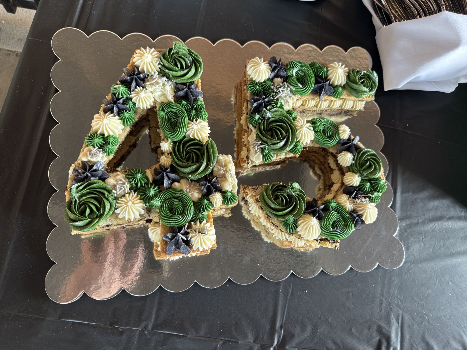 Double-layer number cookie cake for a retirement party with dark green rosettes and cream and black star piping